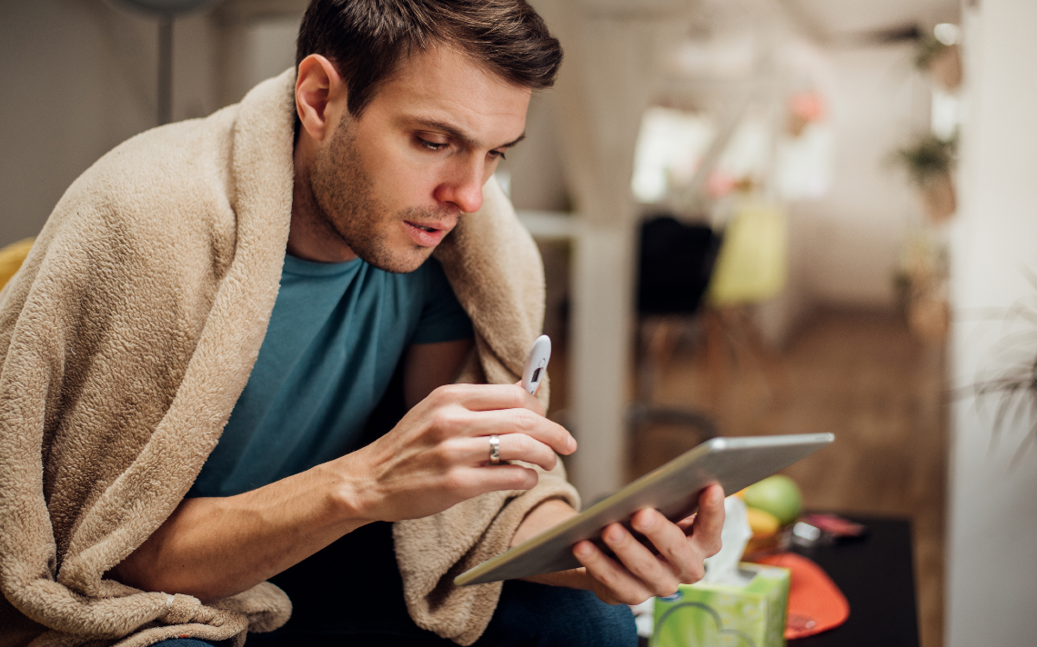 Man with thermometer checking symptoms on ipad